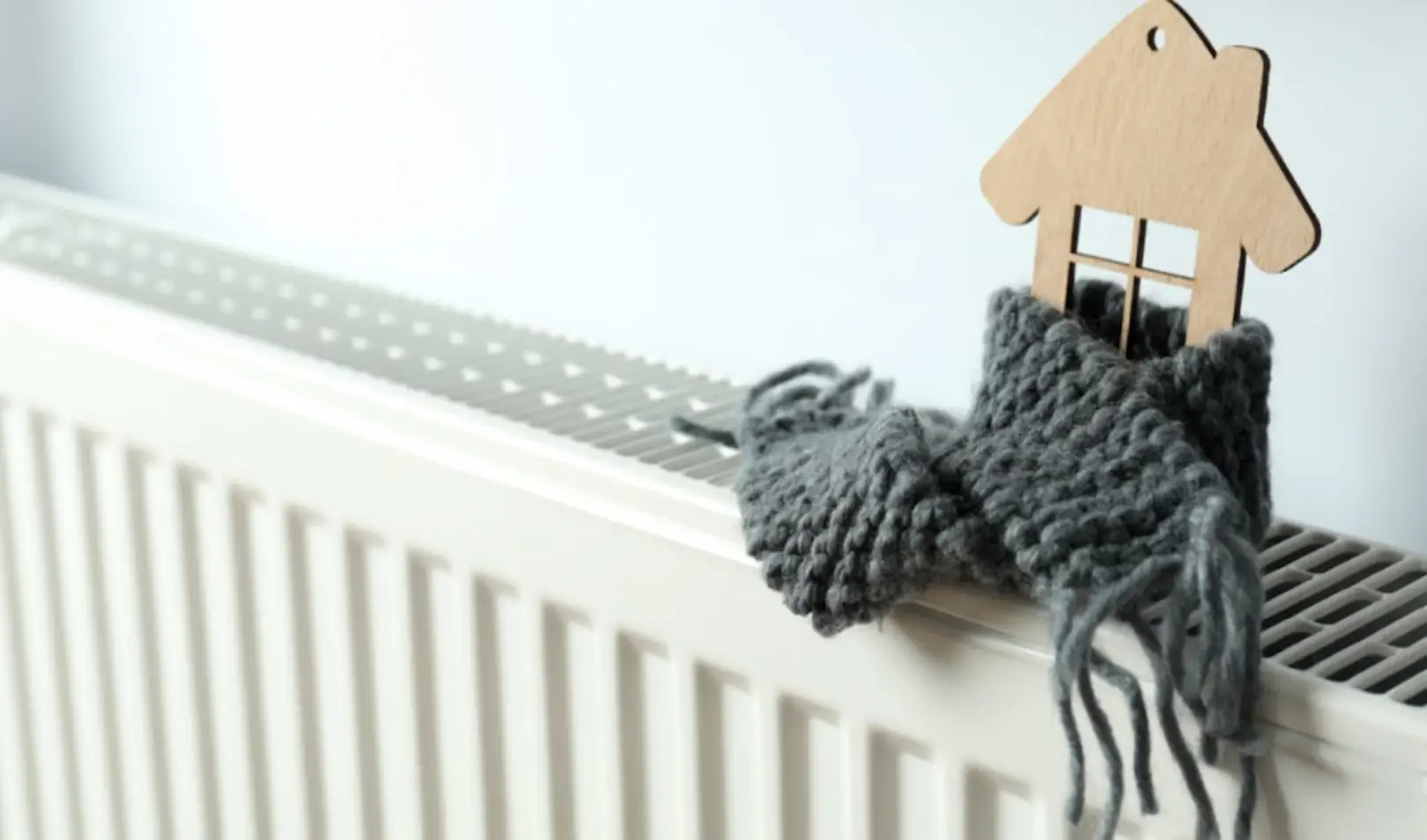 Drveni ukras/ikona kuće omotan sivim šalom na radijatoru